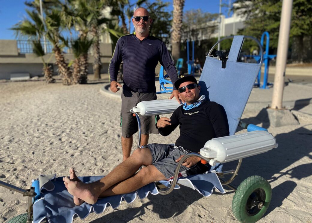 El experto en mecánica automotriz, Andrés Mata (i), y el prestador de servicios turísticos, Jairo Westle, posan junto a una silla de ruedas anfibia.