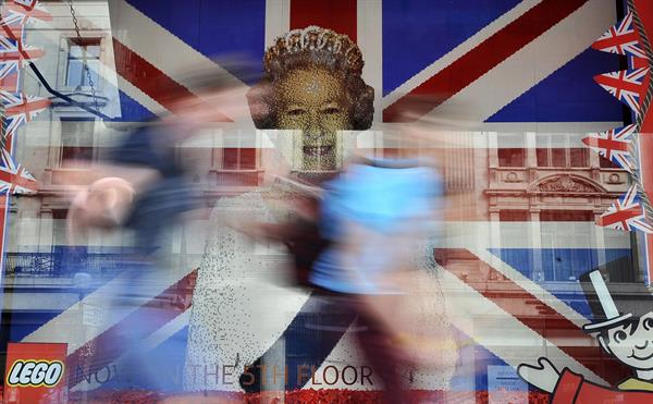Memoria. Unos niños corren frente a una imagen de la difunta reina Isabel II. EFE