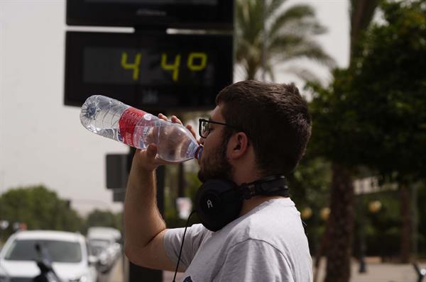 EXTREMO. Un hombre bebe agua junto a un termómetro de calle que marca 44º