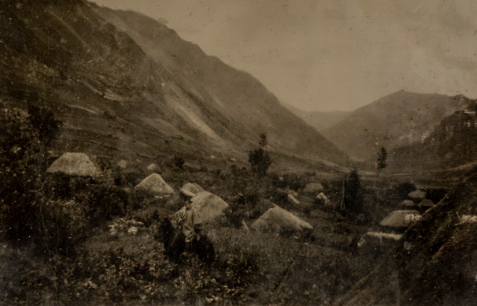 Un jinete posa entre varias chozas en medio de las montañas.