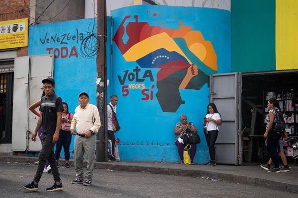 Realidad. Transeúntes caminan frente a un mural con el mapa de Venezuela.