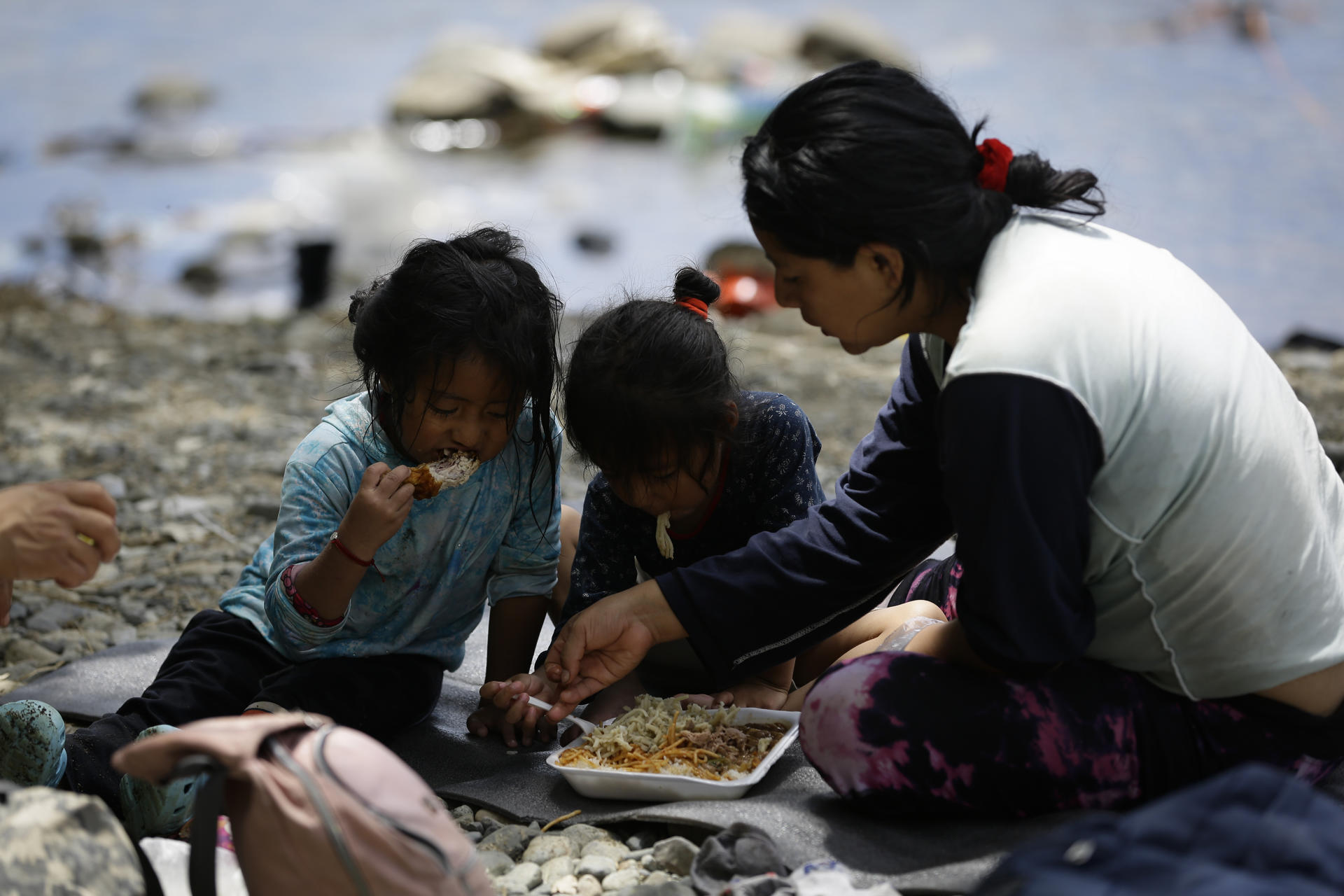 Una migrante ecuatoriana come junto a sus hijas en la selva del Darién mientras esperan para ser trasladados en canoa más al norte.